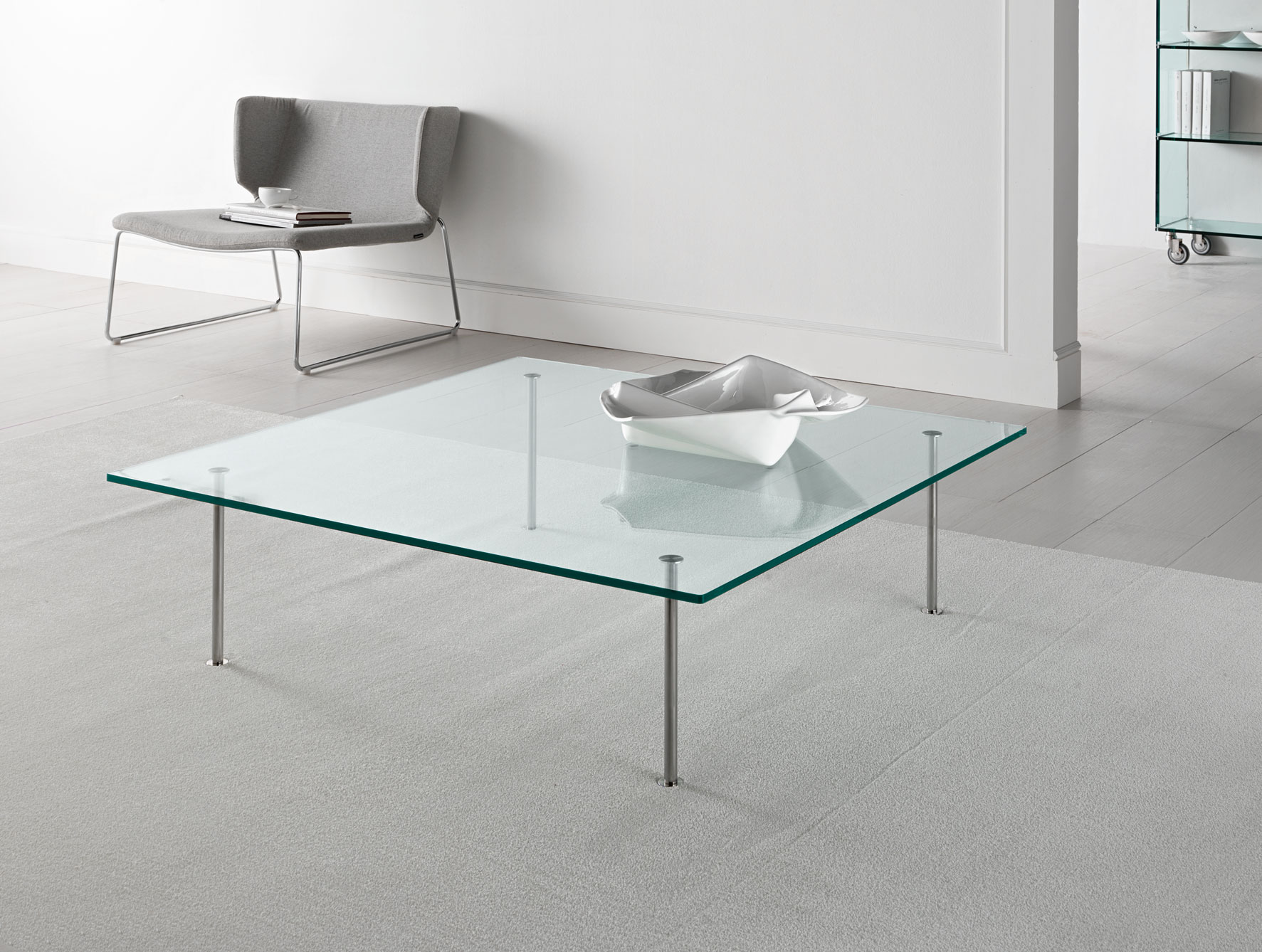 Square glass coffee table with chrome legs in a minimalist white room